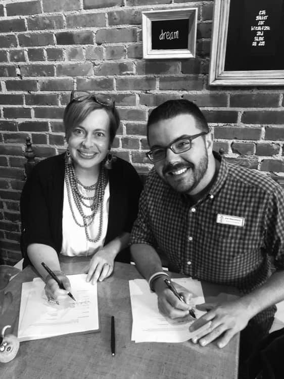 Signing the contract at one of their favorite writing spots, Downtown Deli and Donuts in Spartanburg.